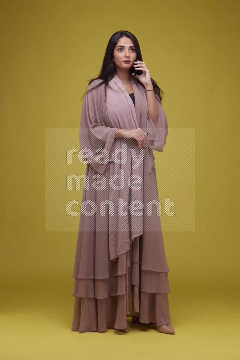 A woman Calling on a Yellow Background wearing Brown Abaya