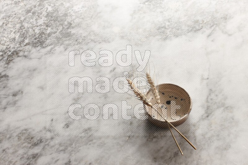 Wheat stalks on multicolored pottery bowl on grey marble background