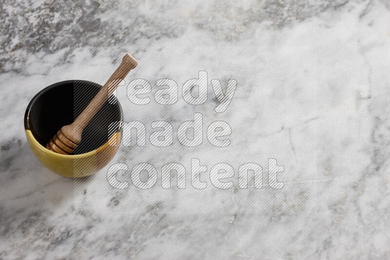 Multicolored pottery bowl with wooden honey dipper in it on grey marble background