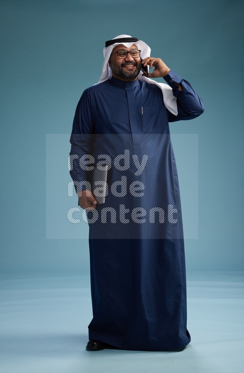 Saudi Man with shimag Standing talking on phone on blue background