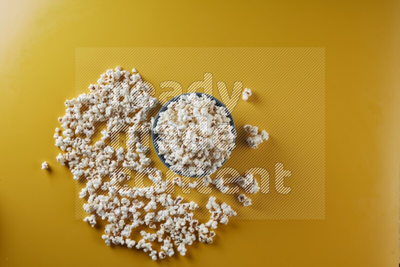 A blue pottery bowl full of popcorn with popcorn beside it on a yellow background in different angles