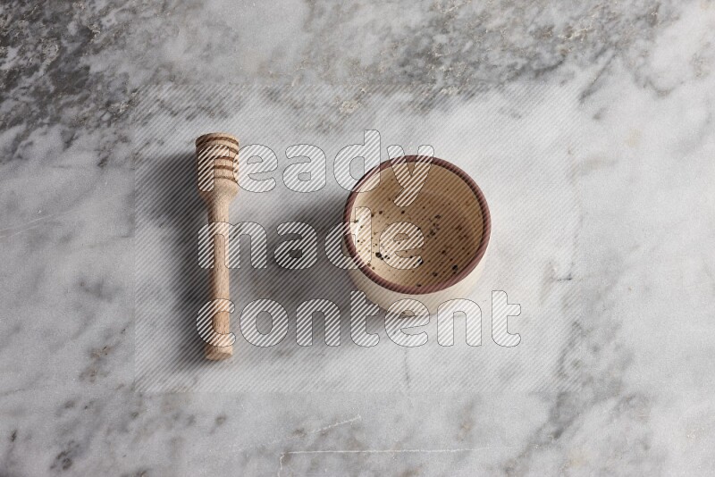 Multicolored pottery bowl with wooden honey dipper on the side on grey marble background