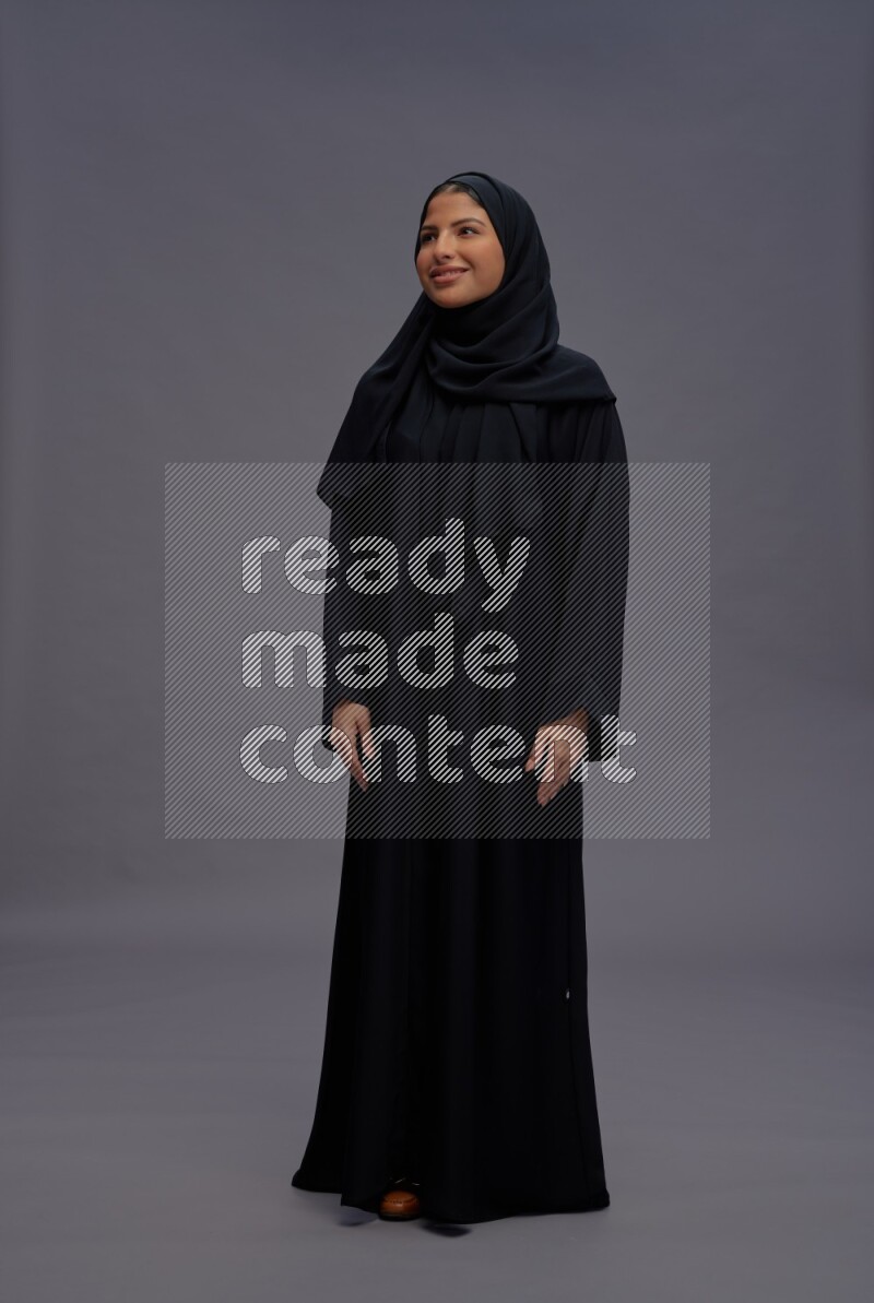 Saudi woman wearing Abaya standing interacting with the camera on gray background