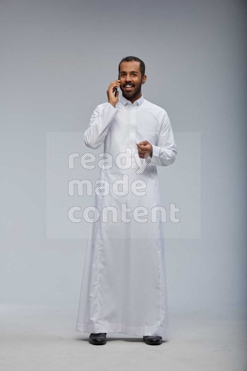 Saudi man wearing Thob standing talking on phone on Gray background