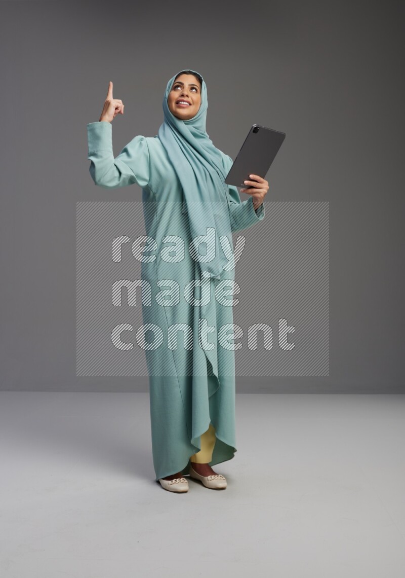 Saudi Woman wearing Abaya standing working on tablet on Gray background