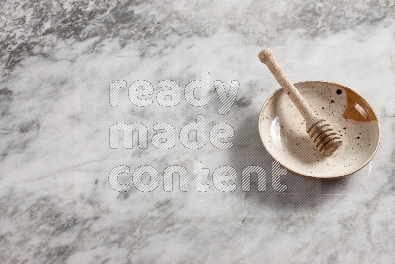 Multicolored pottery plate with wooden honey dipper in it on grey marble background