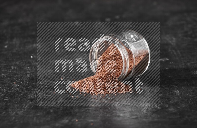 وعاء زجاجي مقلوب ممتلئ ببذور حب الرشاد وتناثرت البذور منه على أرضية سوداء