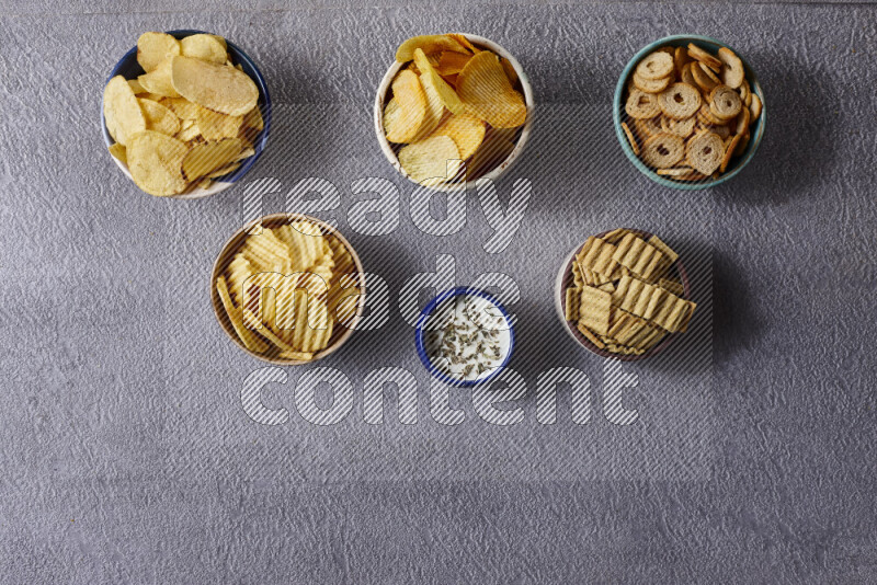 Assorted snacks in pottery bowls on grey background