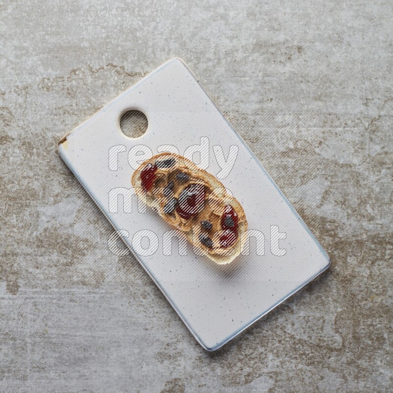 open faced peanut butter sandwich with jam and dried cranberries on a grey textured background