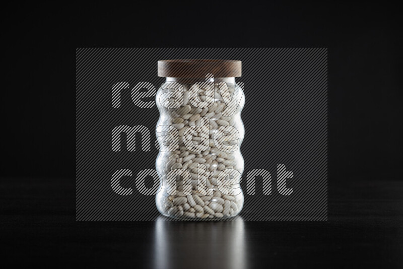 White beans in a glass jar on black background