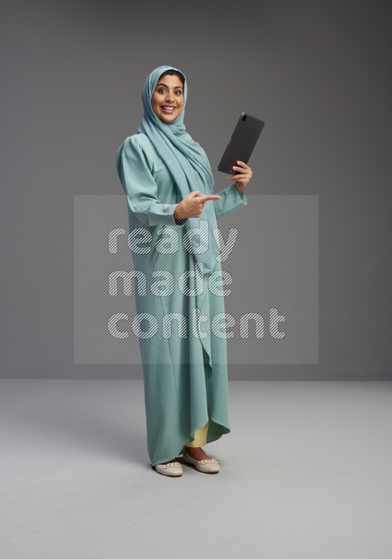 Saudi Woman wearing Abaya standing working on tablet on Gray background