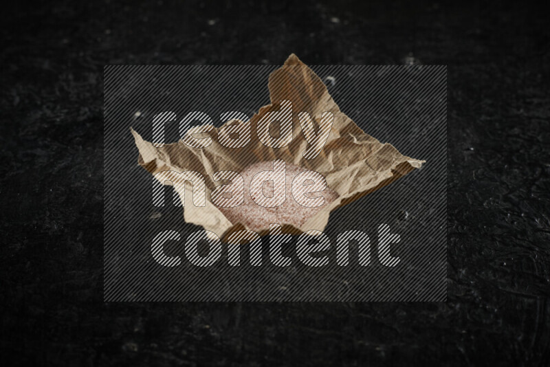 A crumpled piece of paper full of pink himalayan salt on black background