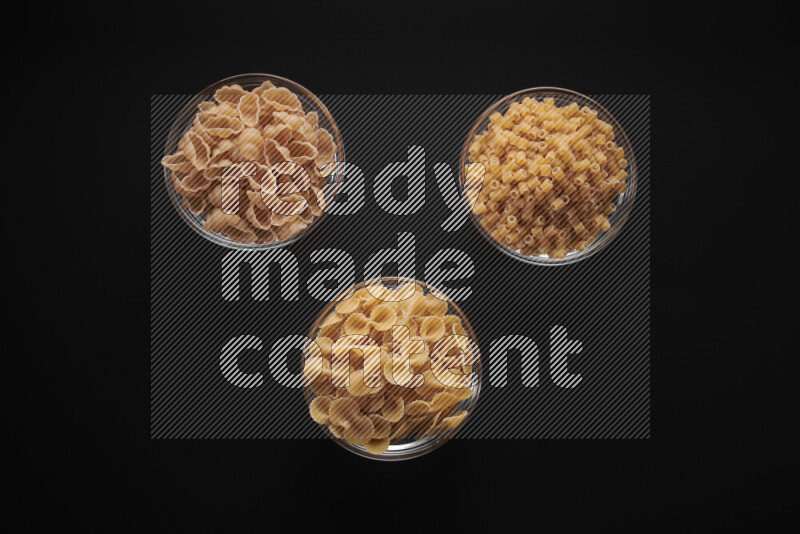 Different pasta types in glass bowls on black background