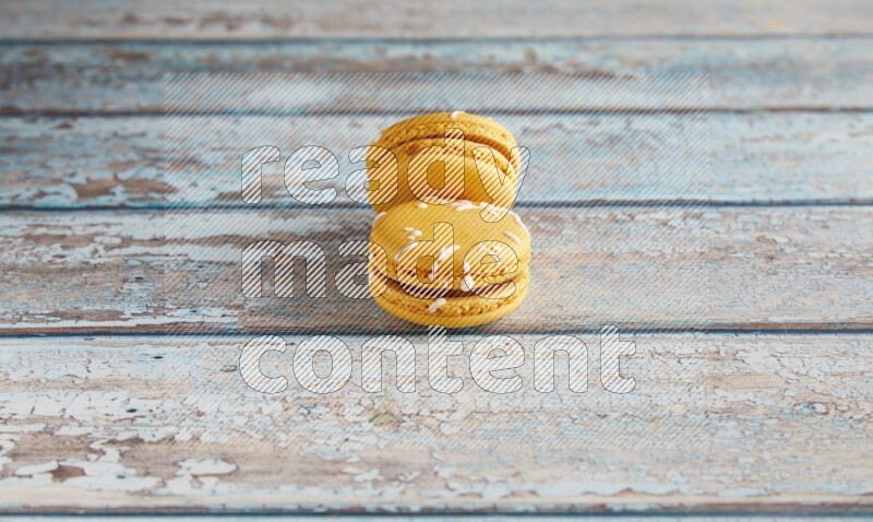 45º Shot of two Yellow Piña Colada macarons on light blue wooden background
