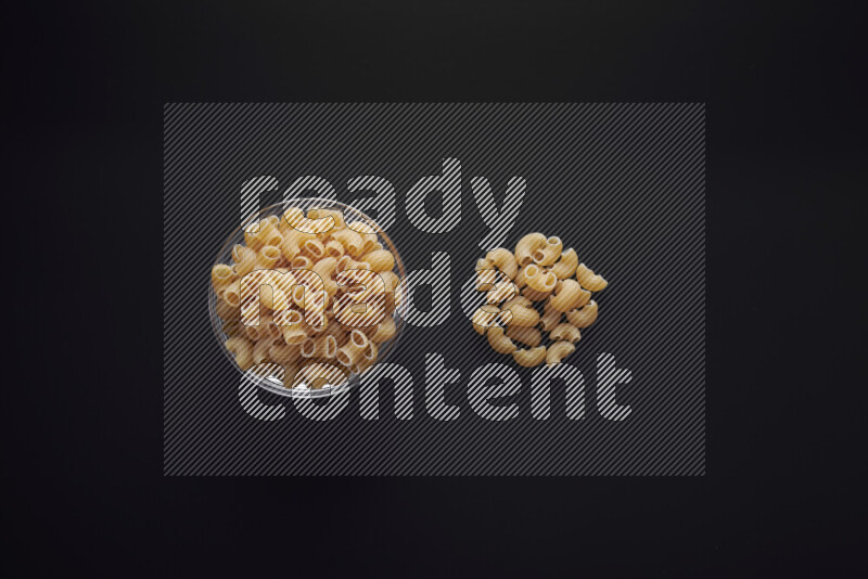 Elbow pasta in a glass bowl on black background