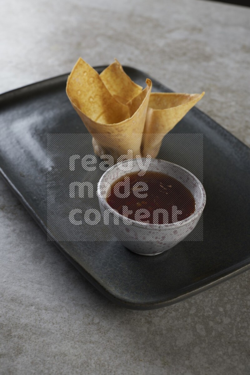 wonton cups with soy sauce ramkin on rectangle dark grey ceramic plate on grey textured counter top