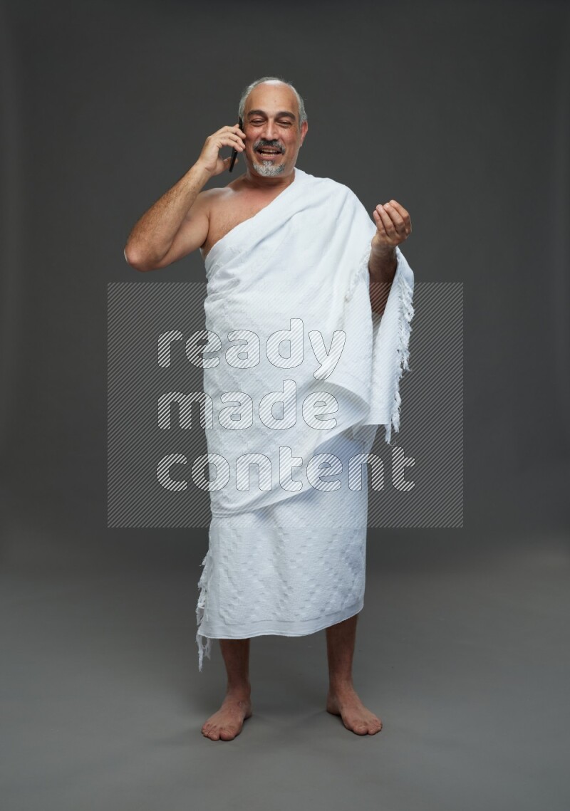 A man wearing Ehram Standing talking on phone on gray background