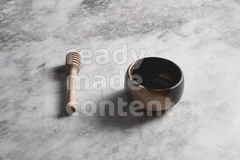 Multicolored pottery bowl with wooden honey dipper on the side on grey marble background