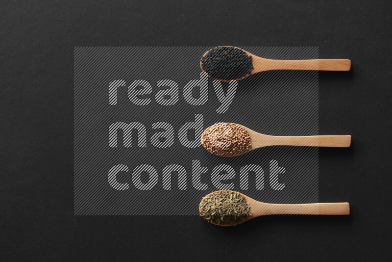 wooden spoons filled with white peppers, mustard seeds, black seeds, garden cress, cumin and flax on black flooring