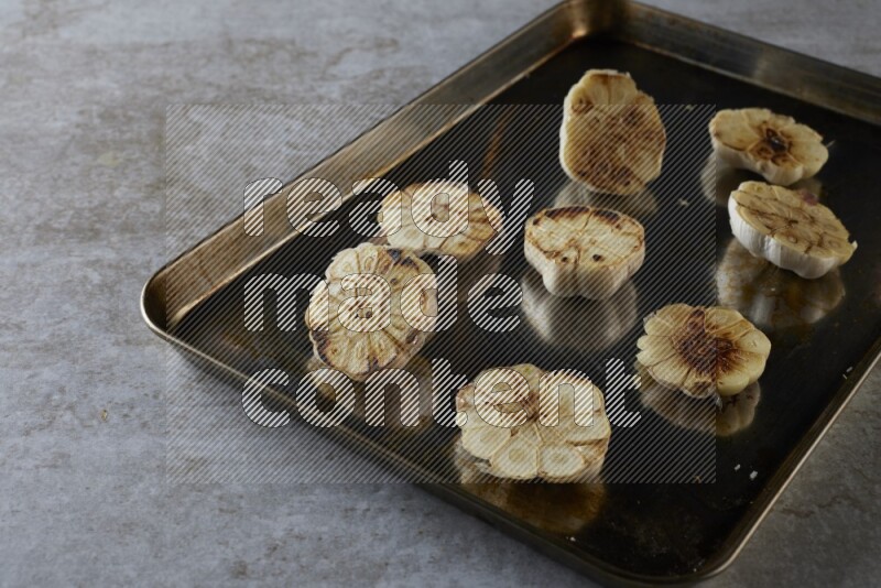 half's roasted garlic in a stainless tray on a grey textured countertop