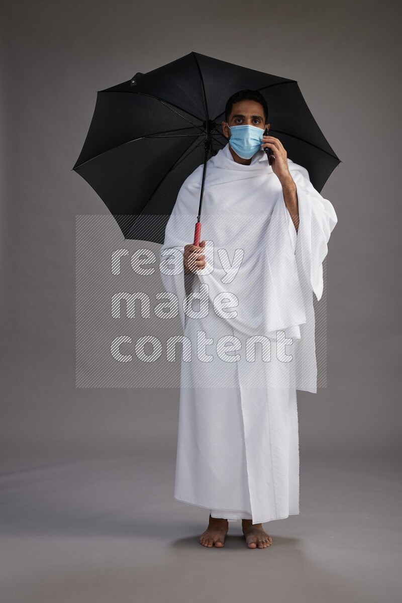 A man wearing Ehram and mask Standing holding umbrella on gray background on gray background