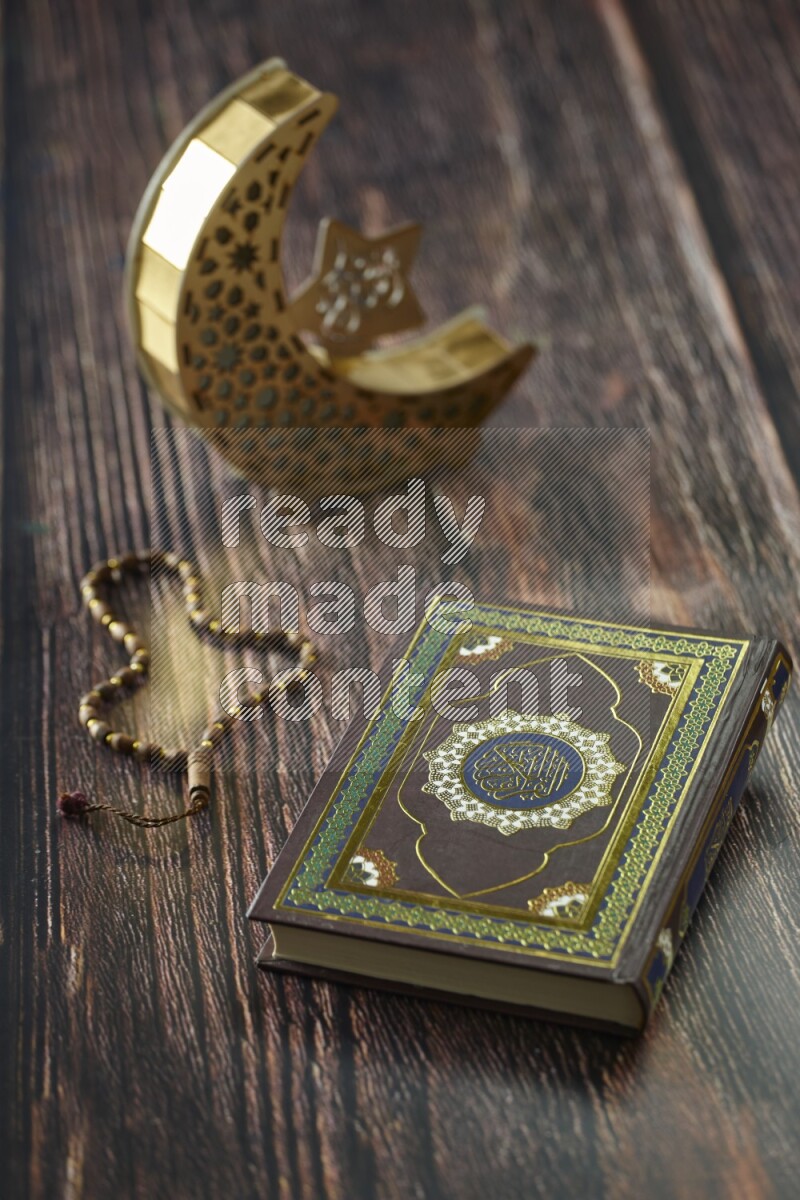 A wooden golden crescent lantern with different drinks, dates, nuts, prayer beads and quran on brown wooden background