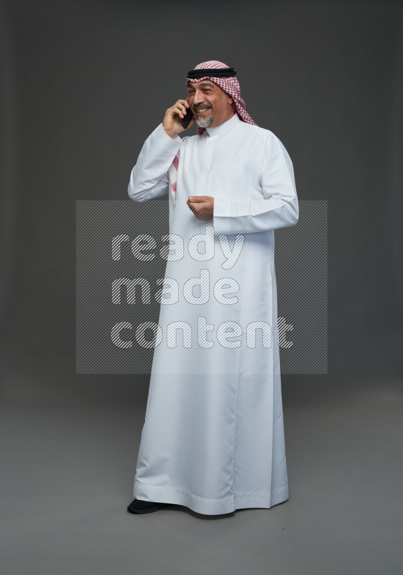 Saudi man with shomag Standing talking on phone on gray background