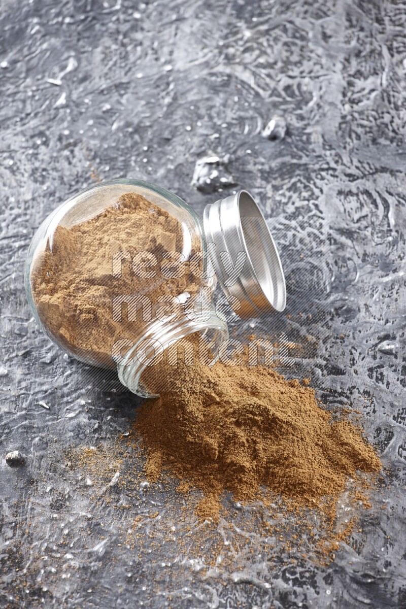 Flipped herbal glass jar full of cinnamon powder on textured black background