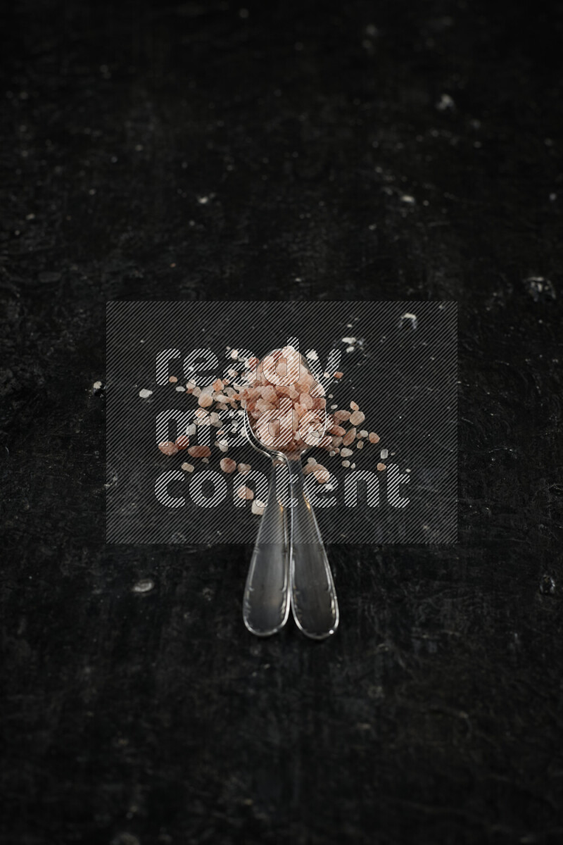 2 metal spoons filled with pink himalayan salt on black background