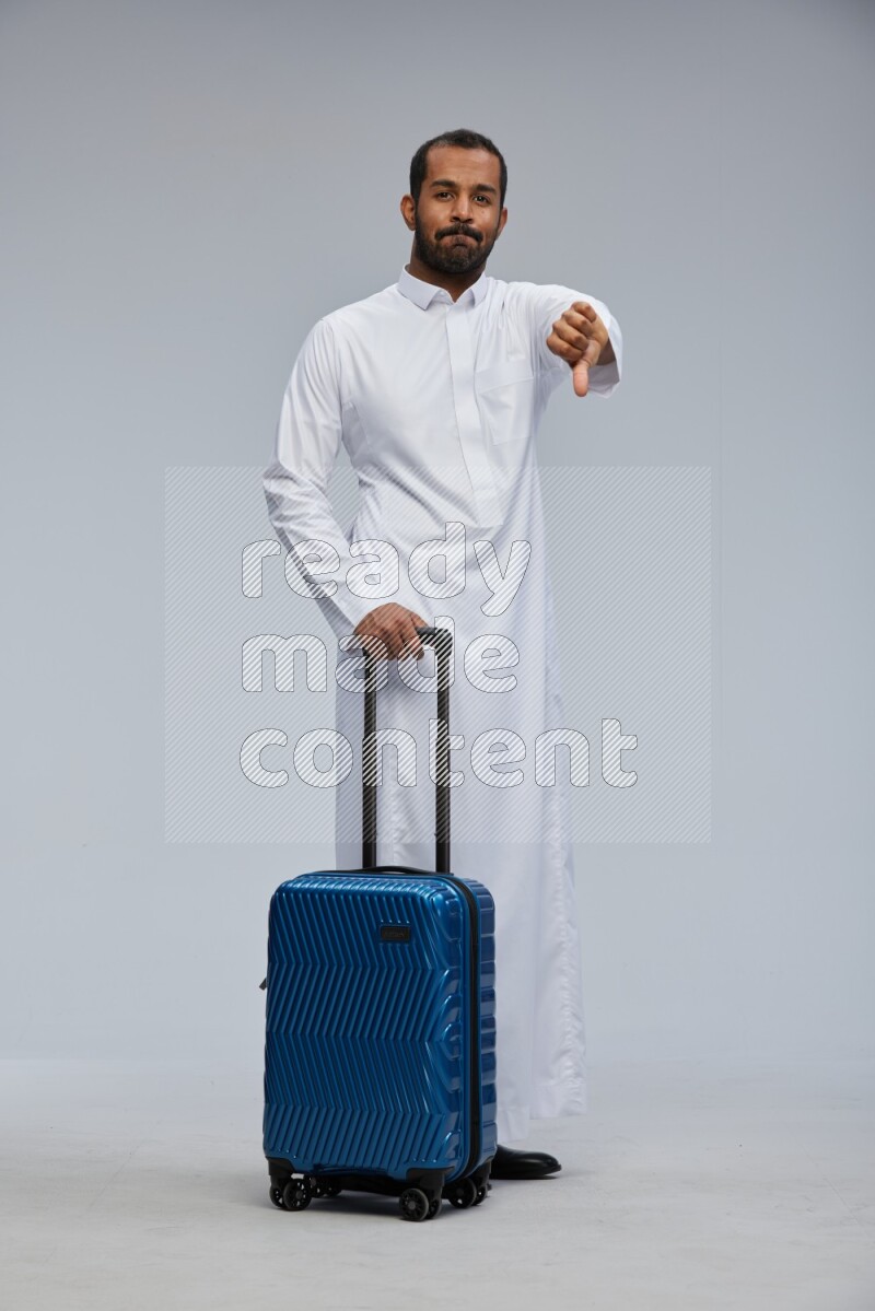 Saudi man wearing thob standing holding Travel bag on Gray background