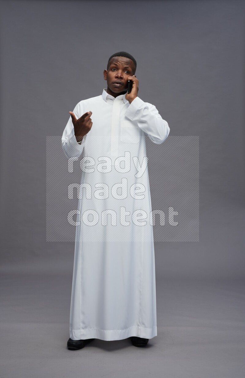 Saudi man wearing thob standing talking on phone on gray background