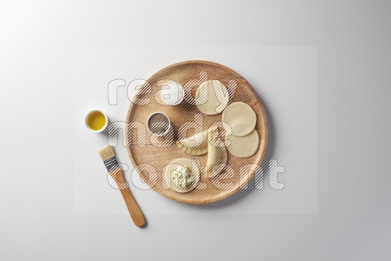 two closed sambosas and one open sambosa filled with cheese while salt, black pepper and oil with oil brush aside in a wooden dish on a white background