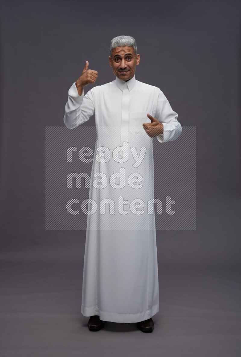 Saudi man wearing thob standing interacting with the camera on gray background