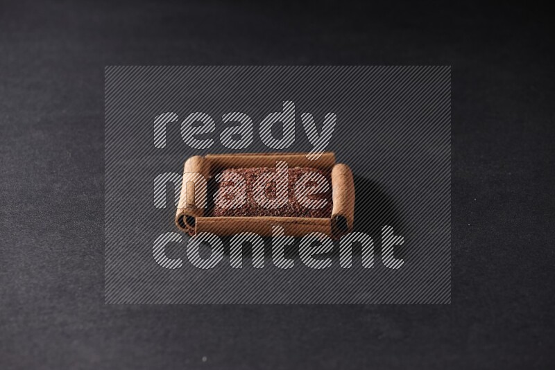 أربعة من أعواد القرفة مكونة شكل مربع بداخلها حب الرشاد علي خلفية سوداء