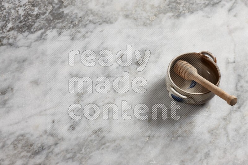 Multicolored pottery bowl with wooden honey dipper in it on grey marble background