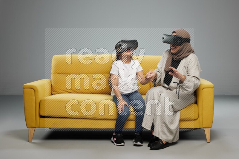 A girl and her mother sitting playing with VR on gray background