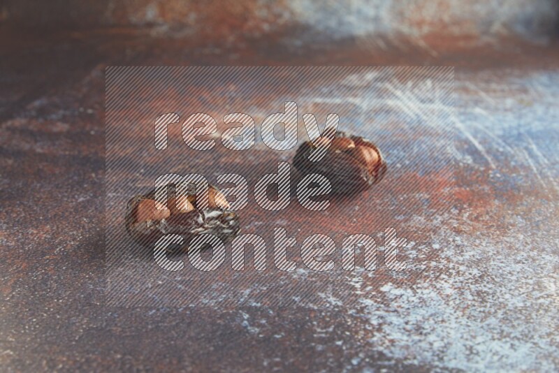 two hazelnut stuffed madjoul dates on a rustic reddish background