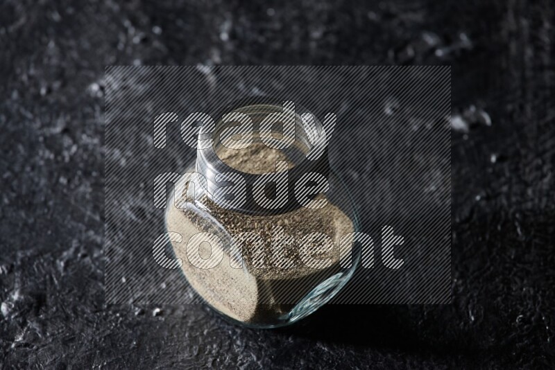 Herbal glass jar full of white pepper on textured black flooring