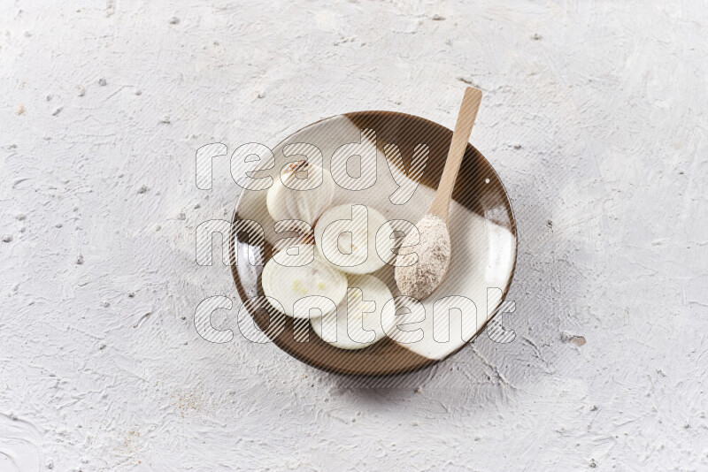 A wooden spoon full of onion powder with sliced onions, all on a pottery plate on white background