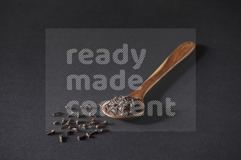 A wooden ladle full of whole cloves on a black flooring