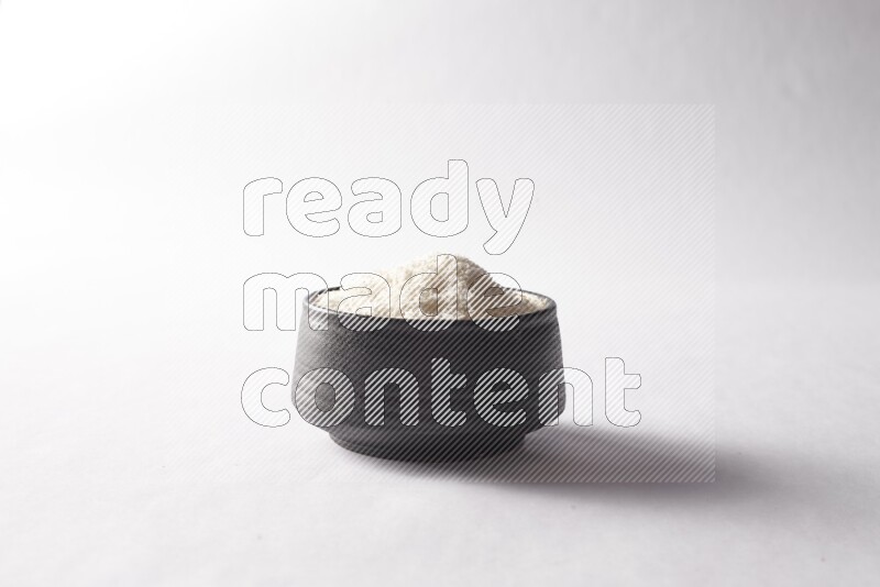 Desiccated coconuts in a black pottery bowl on white background