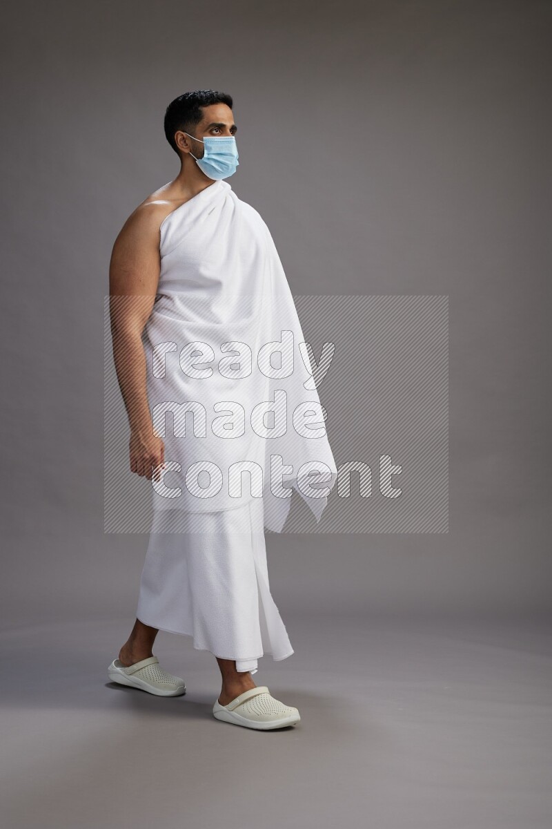 A man wearing Ehram with face mask Standing Interacting with the camera on gray background
