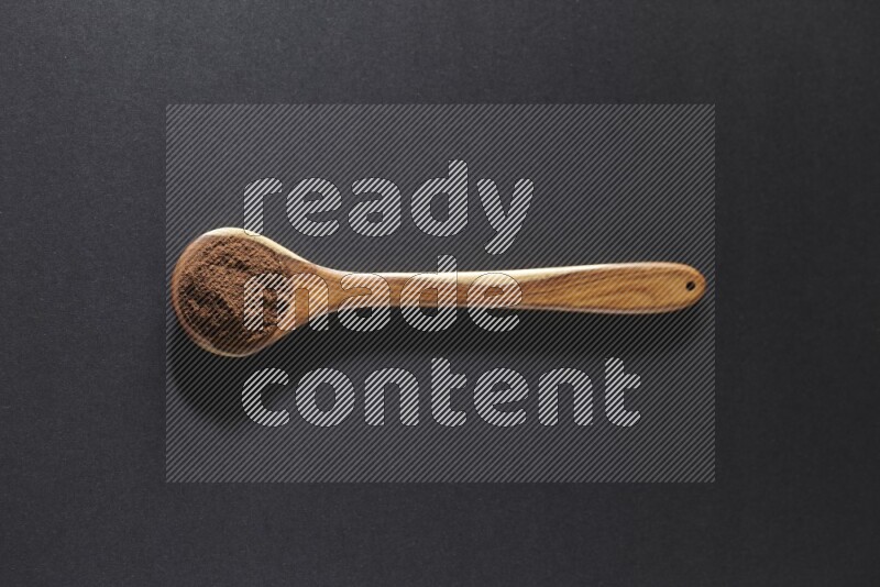 A wooden ladle full of cloves powder on a black flooring