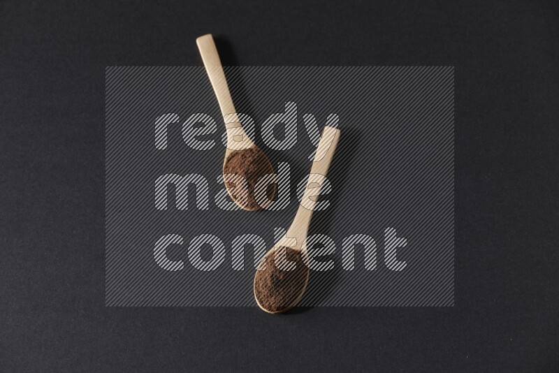 2 wooden spoons full of cloves powder on a black flooring
