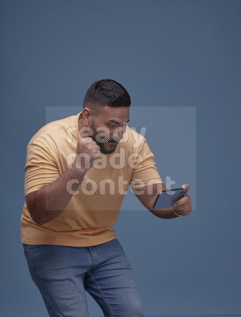 A man Playing Games on Smartphone on Blue Background wearing Orange T-shirt