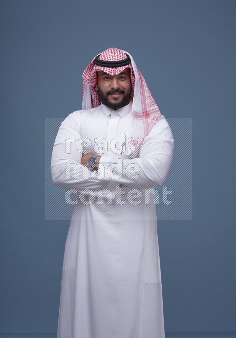A Saudi man posing on blue background wearing Thob and Shomag
