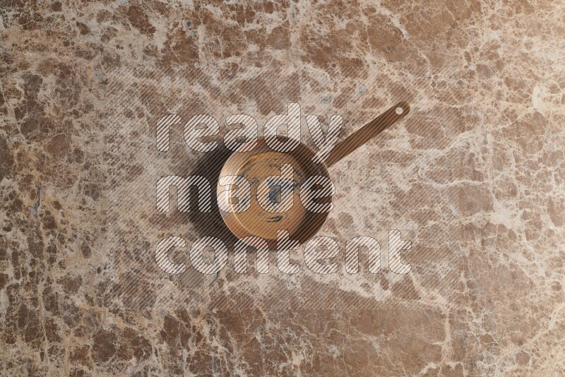 A small copper pan on beige marble background