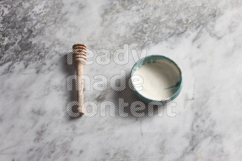 Multicolored pottery bowl with wooden honey dipper on the side on grey marble background