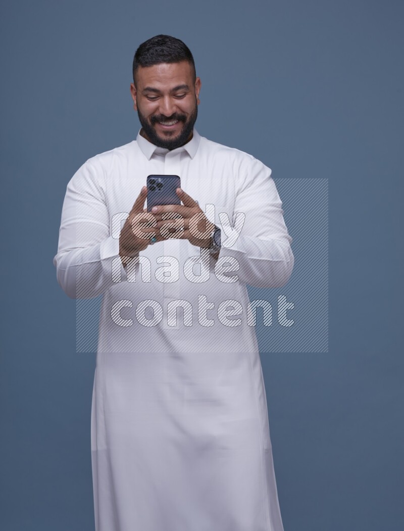 A man Texting on Blue Background wearing Saudi Thob