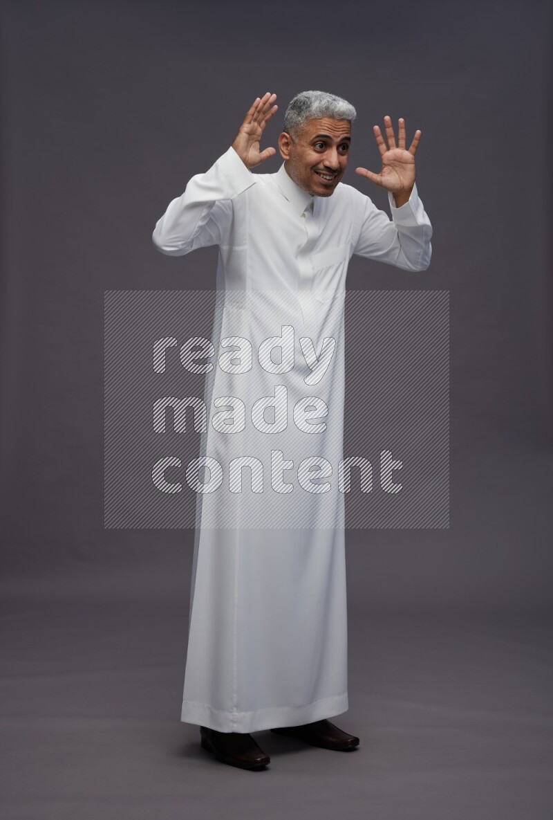 Saudi man wearing thob standing hands behind head on gray background
